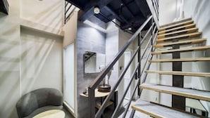 Un intérieur moderne avec un escalier, une table ronde et un fauteuil gris.