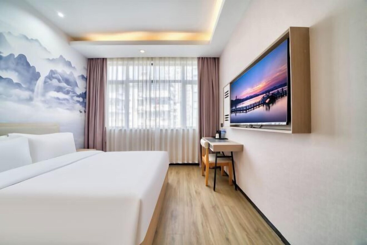 A hotel room with a large bed, a desk, and a painting of a sunset over a bridge.