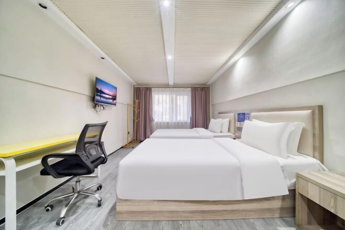 A hotel room with a bed, a desk, a chair, and a TV on the wall.