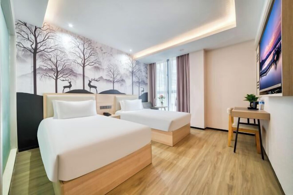 A hotel room with two beds, a desk, a chair, a TV, and a mural on the wall.