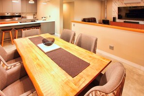 A modern dining area with a wooden table, cushioned chairs, and a kitchen in the background. - Salty Springbok, Langebaan 6-sleeper (Langebaan)