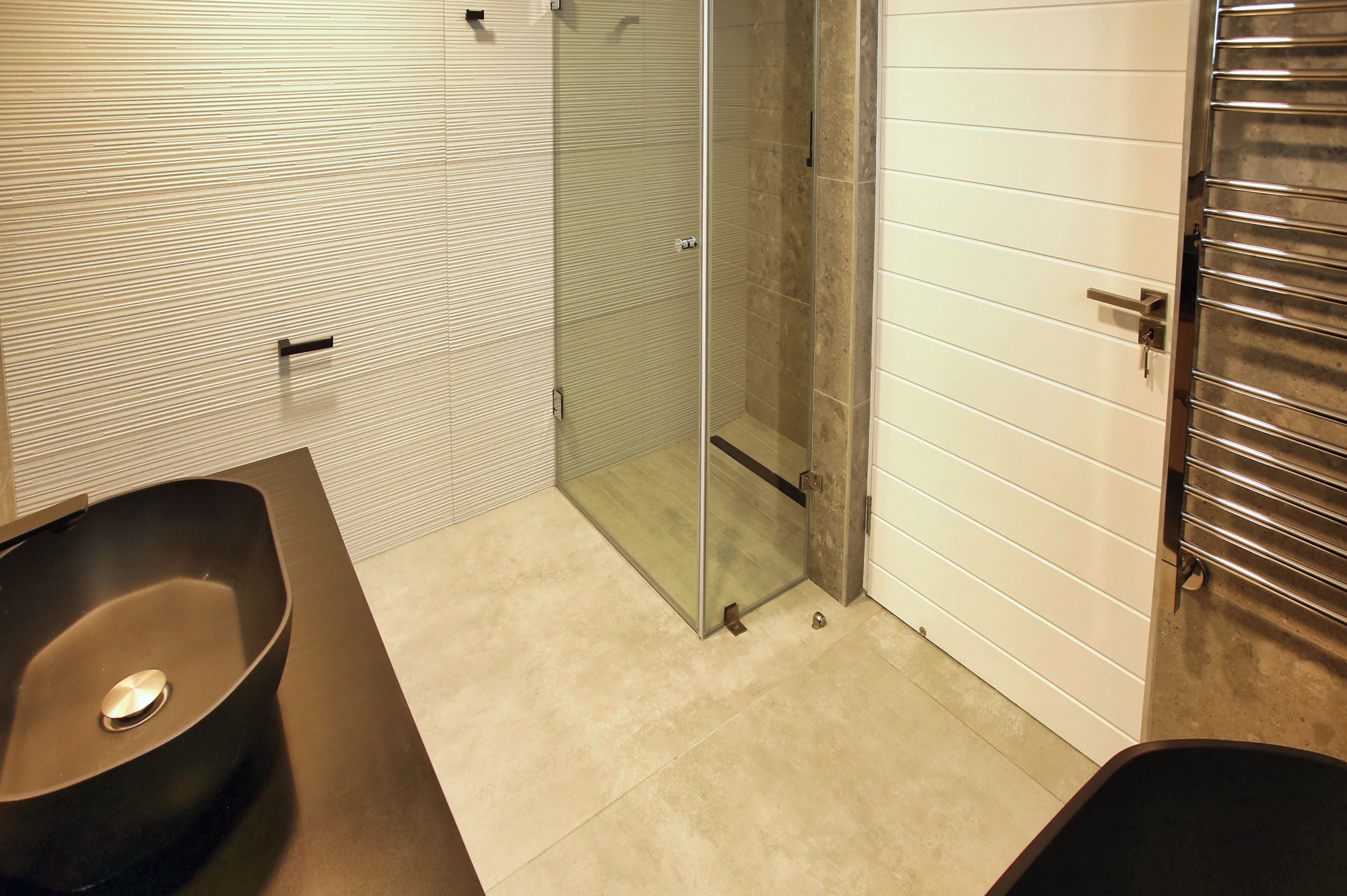 A modern bathroom with a large black sink, a glass shower enclosure, and a white tiled wall.