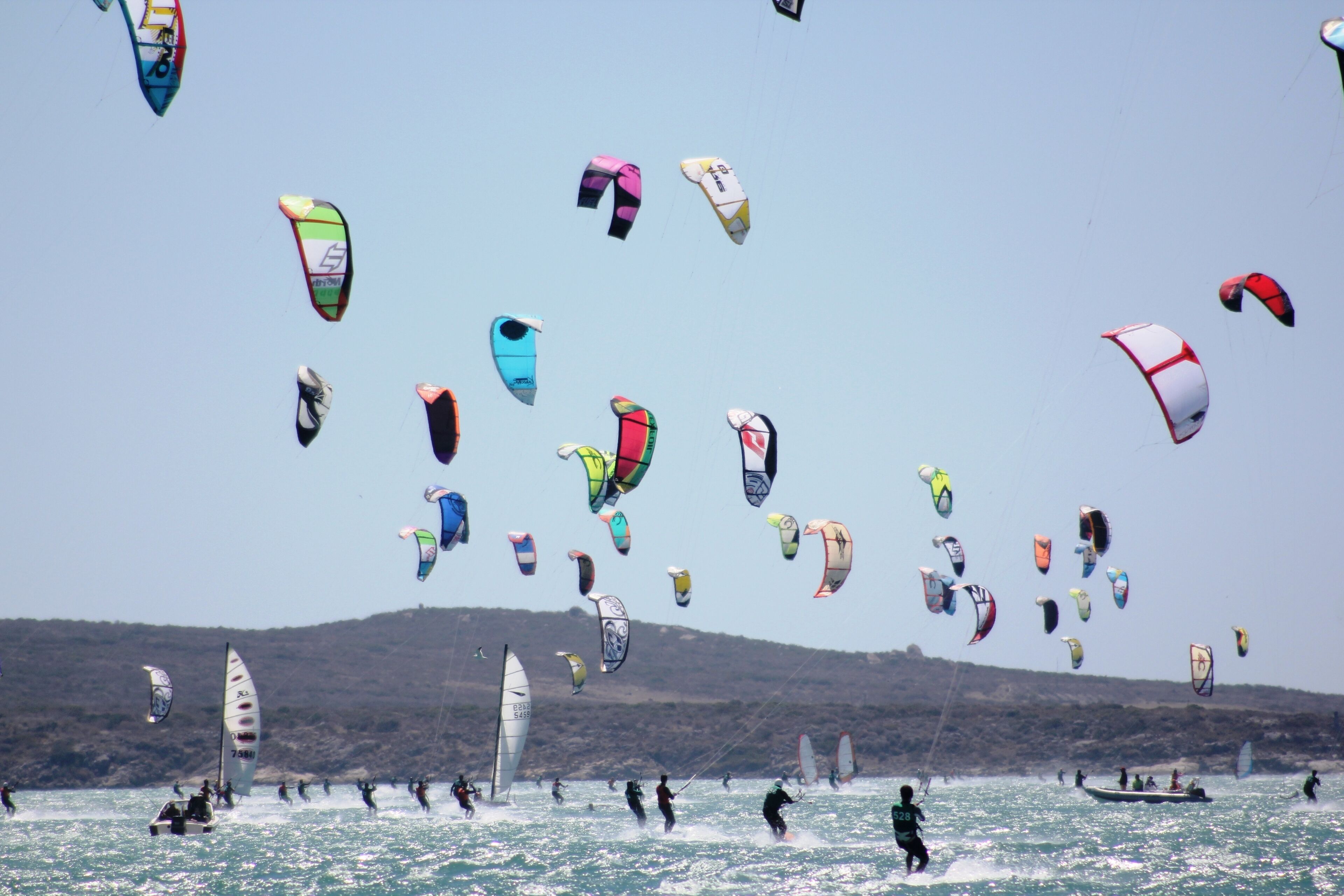 A beach with multiple windsurfing and kiteboarding activities.