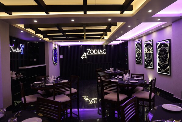 A restaurant interior with tables and chairs, a neon sign, and zodiac-themed wall decorations. - XCELSIOR HOTEL AND SPA BY ROH (Shillong)