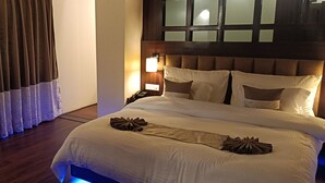 A neatly made bed with a headboard, a bedside lamp, and a window with curtains. - XCELSIOR HOTEL AND SPA BY ROH (Shillong)