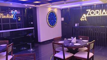 A restaurant with a neon sign reading "Mocktail" and "Zodiac". Tables are set with white tablecloths and silverware.