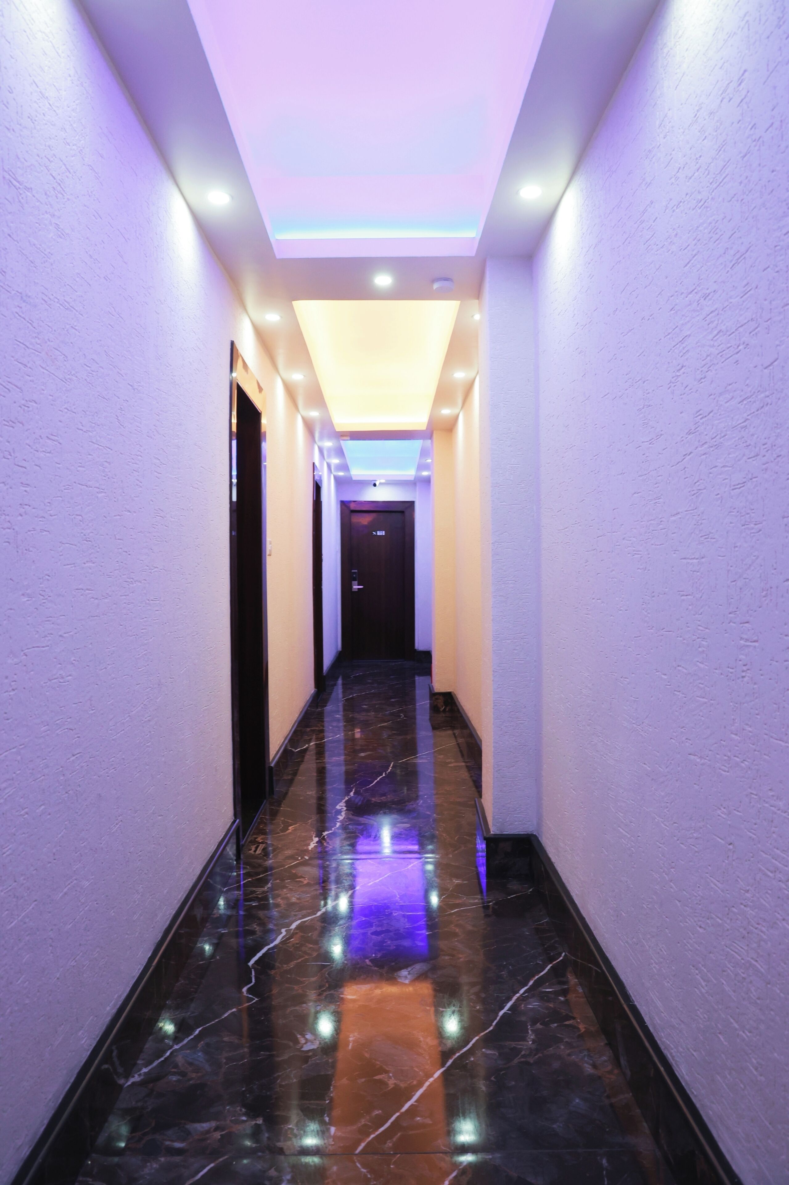A hallway with a reflective marble floor, recessed lighting, and a ceiling with a light fixture.