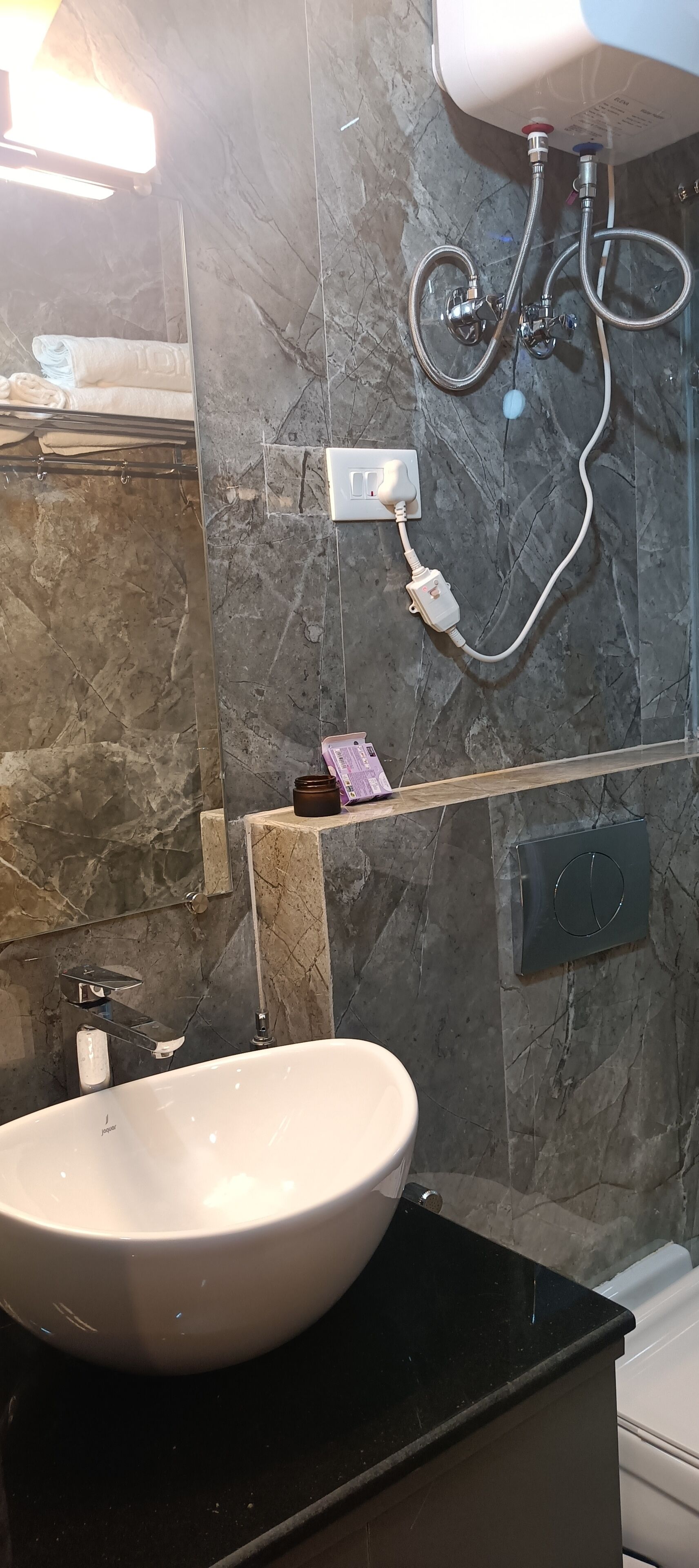 Un baño con lavamanos blanco, paredes de mármol y ducha con tuberías a la vista.