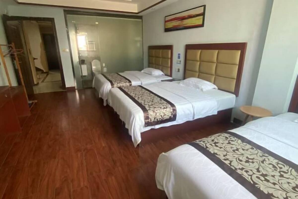 A hotel room with three beds, wooden flooring, and a large window.
