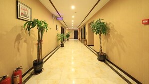 Un couloir d’hôtel avec un sol en marbre poli, des plantes en pot, des œuvres d’art encadrées et un extincteur.
