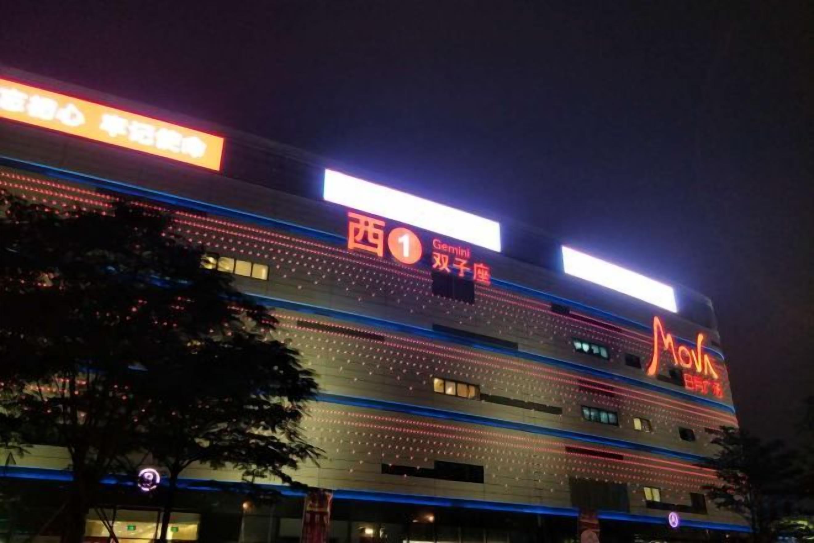Um edifício de vários andares com letreiros iluminados, incluindo um grande letreiro 'Cinema' e um letreiro 'Giant'.