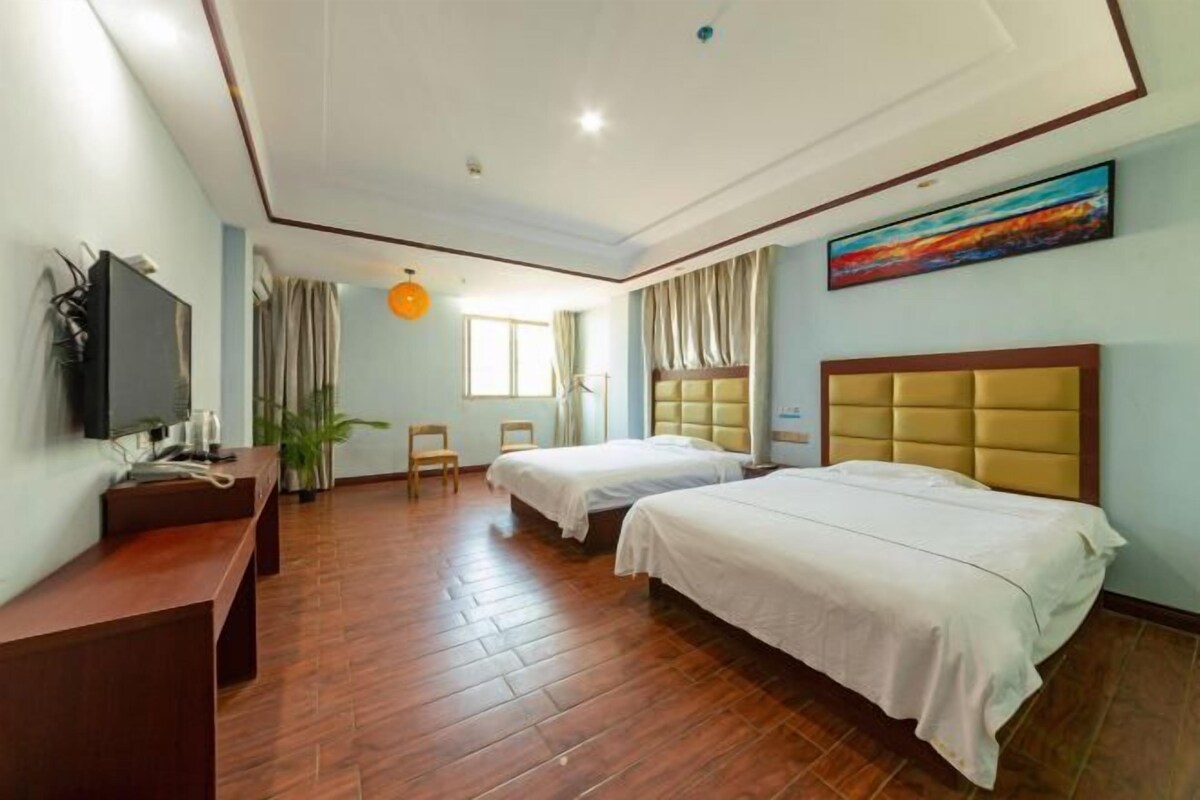 Ein Hotelzimmer mit zwei Betten, einem Schreibtisch, einem Fernseher und einem Gemälde an der Wand.