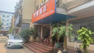 A hotel entrance with a red sign, steps leading up to the door, and a parked car.