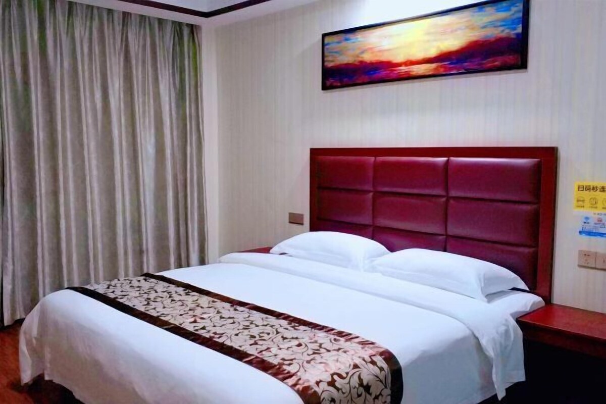A hotel room with a large bed, a red headboard, and a painting on the wall.