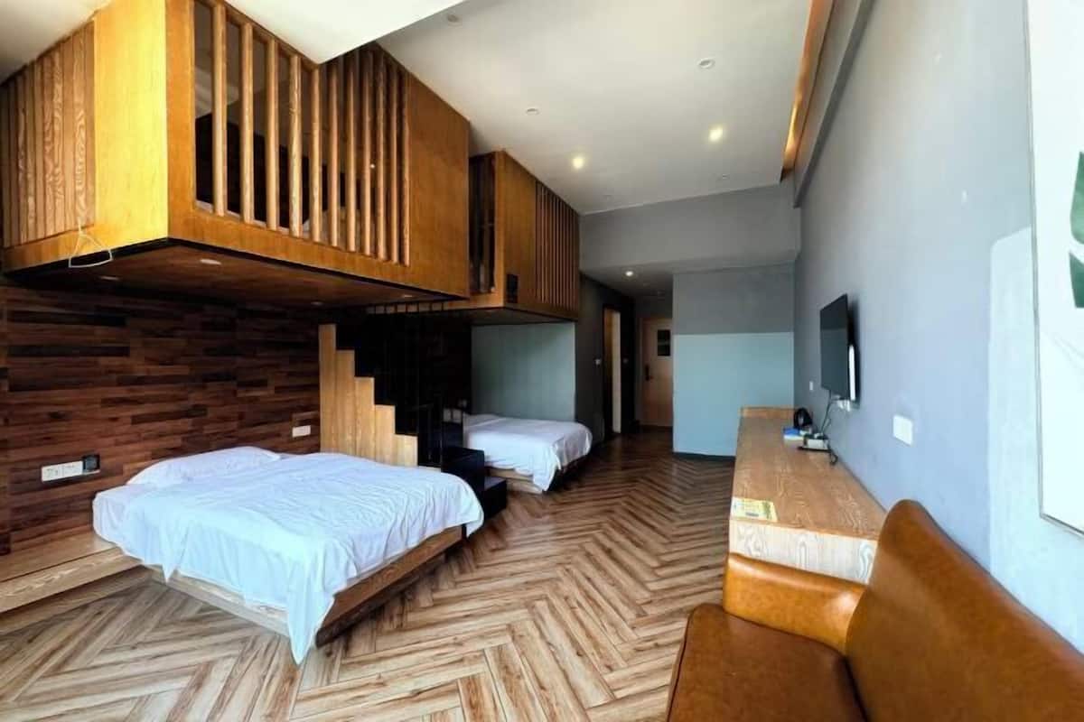 A room with two beds, a wooden slatted ceiling, a TV, and a herringbone-patterned floor.