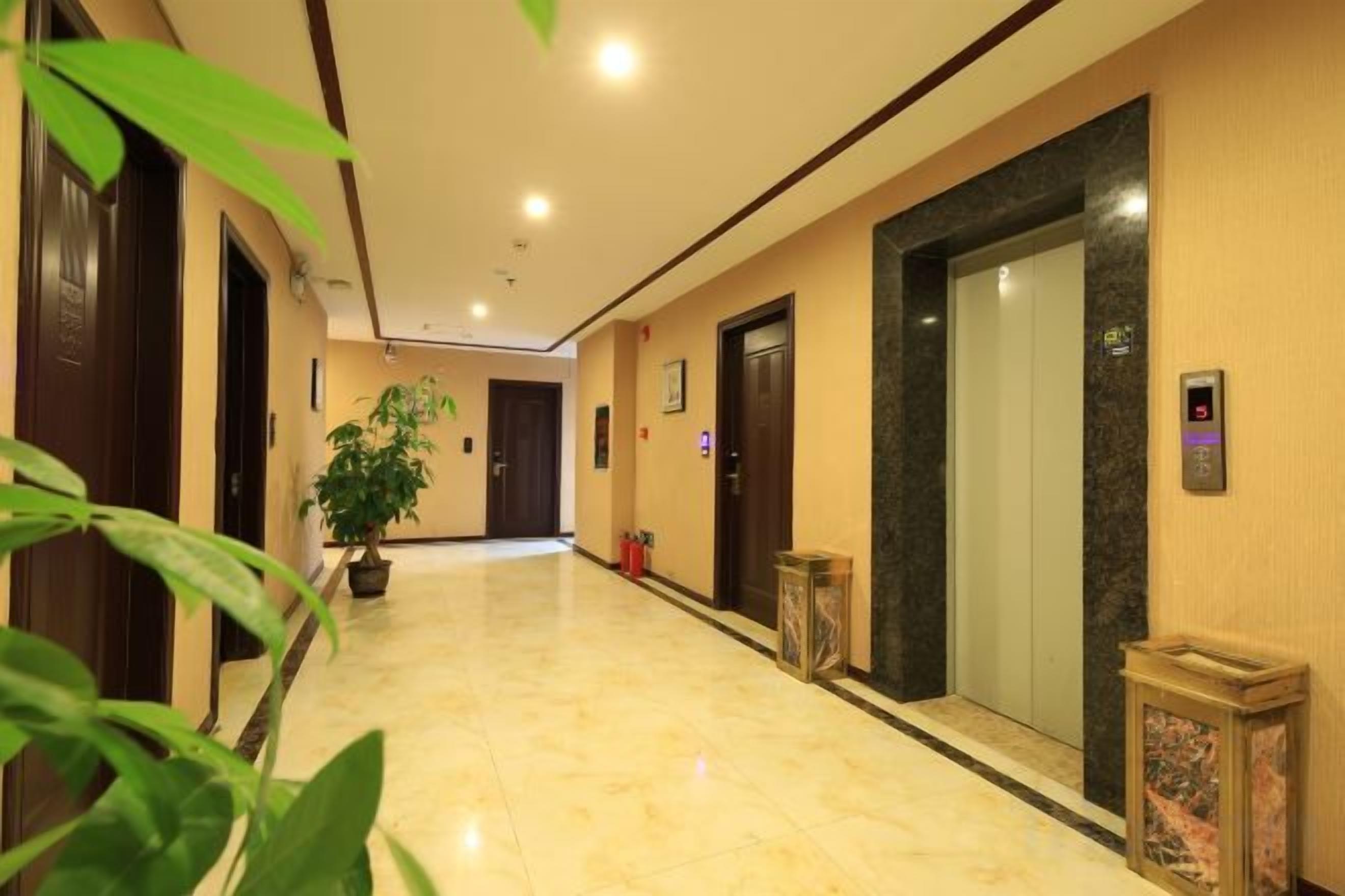 A hotel corridor with a marble floor, a potted plant, an elevator, and a trash bin.