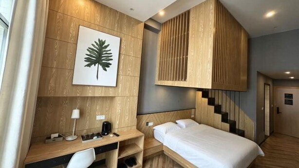 Une chambre d’hôtel avec un lit, un bureau et une chaise, des lambris en bois, une œuvre d’art représentant des feuilles et un escalier.