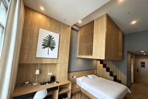 Ein Hotelzimmer mit Bett, Schreibtisch, Stuhl, Holzvertäfelung, einer Blattform-Kunstwerk und einer Treppe.