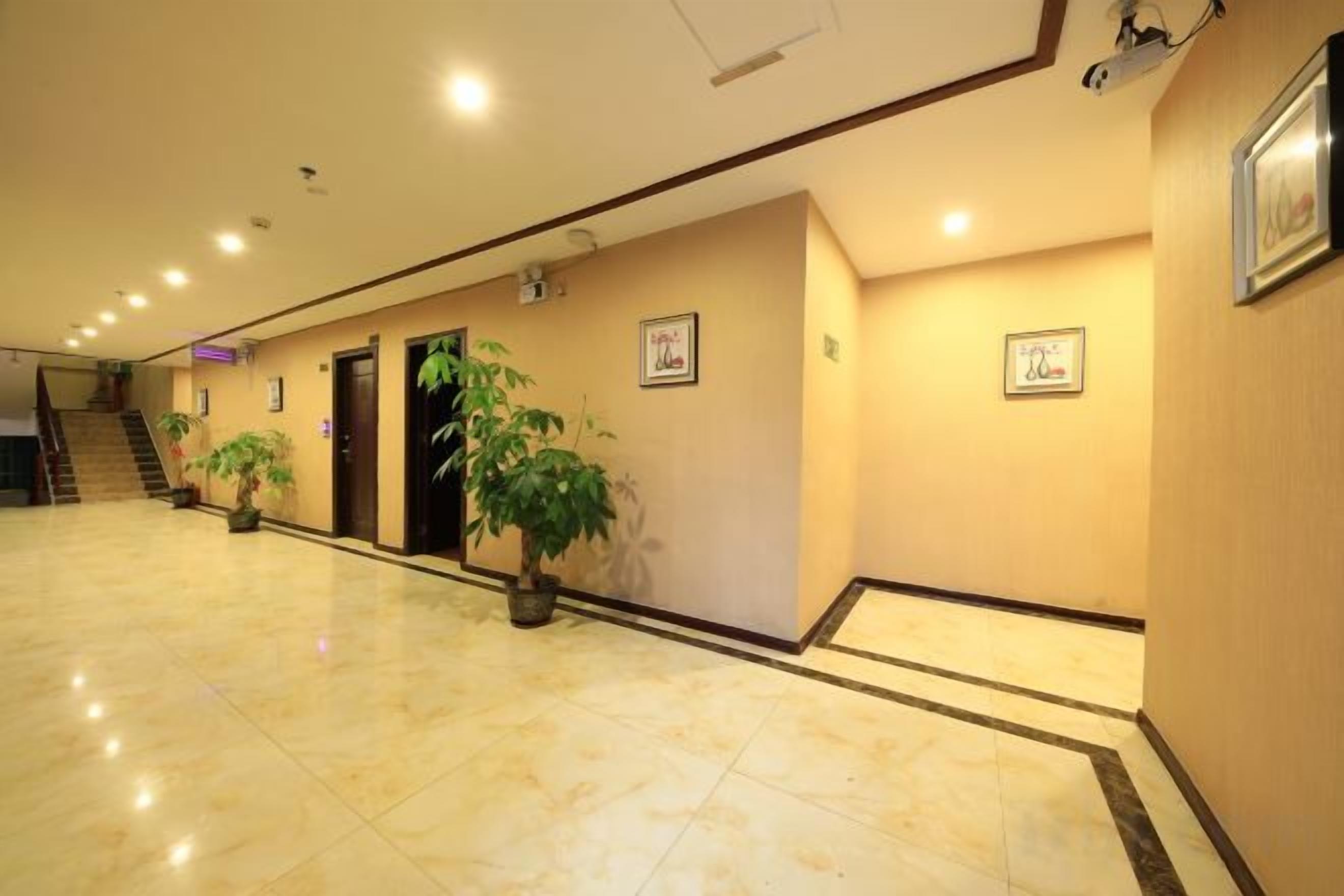 Corredor de hotel com piso de mármore, plantas em vasos, quadros nas paredes e uma escadaria no final.