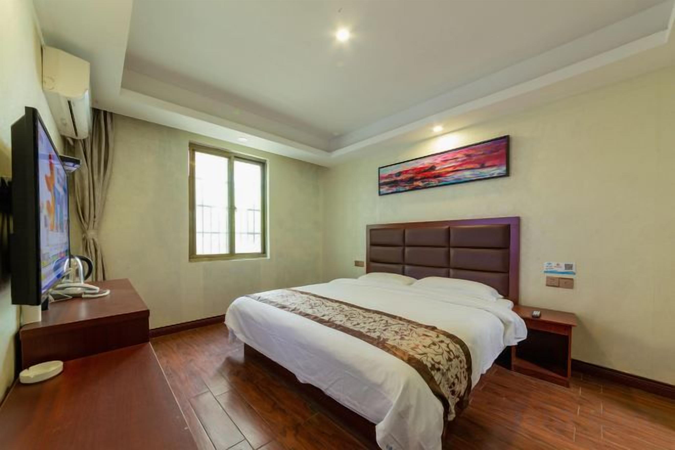 A hotel room with a large bed, a television, a window, and a painting on the wall.