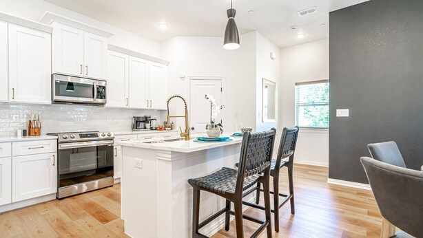 A modern kitchen with white cabinets, stainless steel appliances, and a central island with two chairs. - Cowboys & Rangers Game-Day Townhome | Free Parking (Arlington)