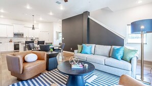 A modern living room with a sofa, armchair, and coffee table. There is a staircase leading to an upper level. - Cowboys & Rangers Game-Day Townhome | Free Parking (Arlington)