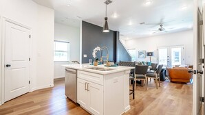 A modern kitchen with white cabinetry, a central island with a sink, and a dining area with a table and chairs. - Cowboys & Rangers Game-Day Townhome | Free Parking (Arlington)