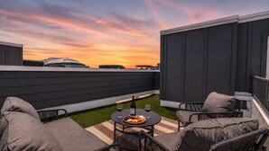 A rooftop patio with outdoor furniture, a table with a bottle of wine, and a plate of snacks. - Cowboys & Rangers Game-Day Townhome | Free Parking (Arlington)