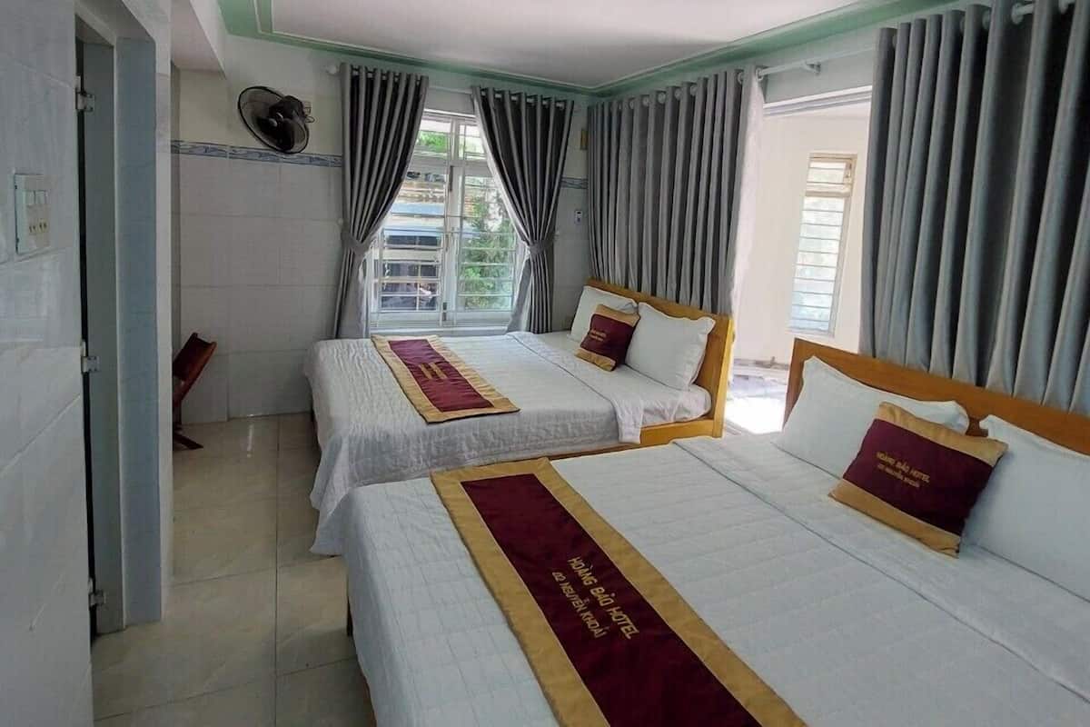 A hotel room with two beds, a window with curtains, a wall-mounted fan, and a tiled floor.
