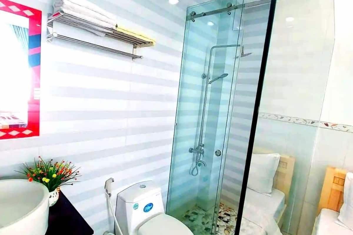 A modern bathroom with a glass shower enclosure, a white toilet, and a sink with a red trash bin.