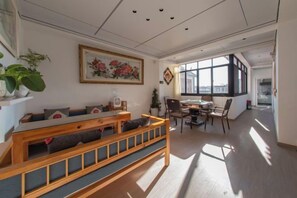 A modern living room with a wooden bench, a dining table with chairs, a large window, and a painting on the wall.