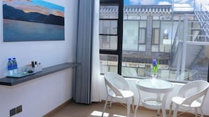 A hotel room with a large window, a painting, a small table with chairs, and a water bottle on the window sill.