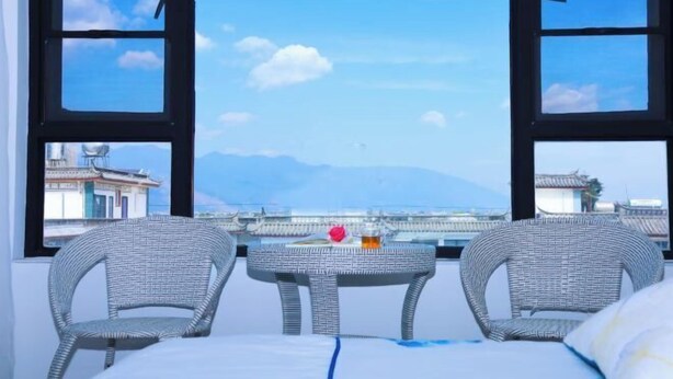 A room with a view of a bridge and mountains, featuring wicker furniture and a small table with a drink.