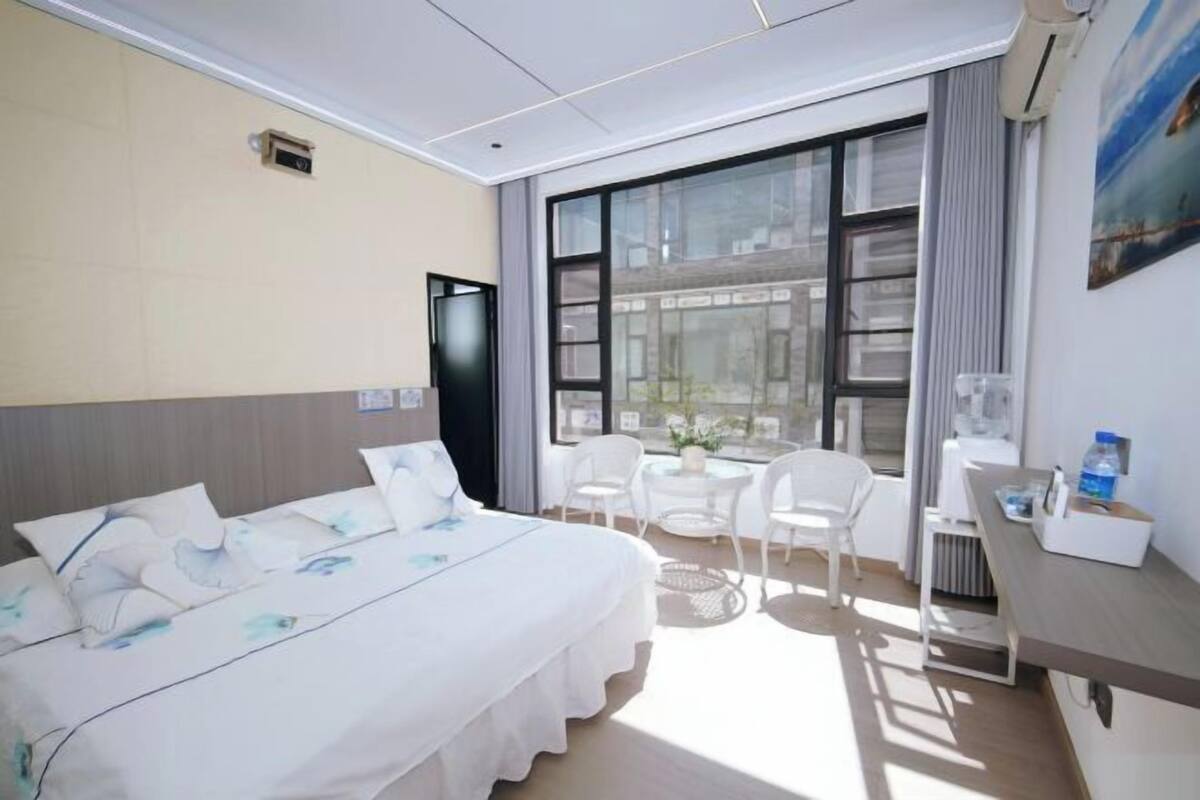 A hotel room with a bed, a desk, a chair, and a large window.