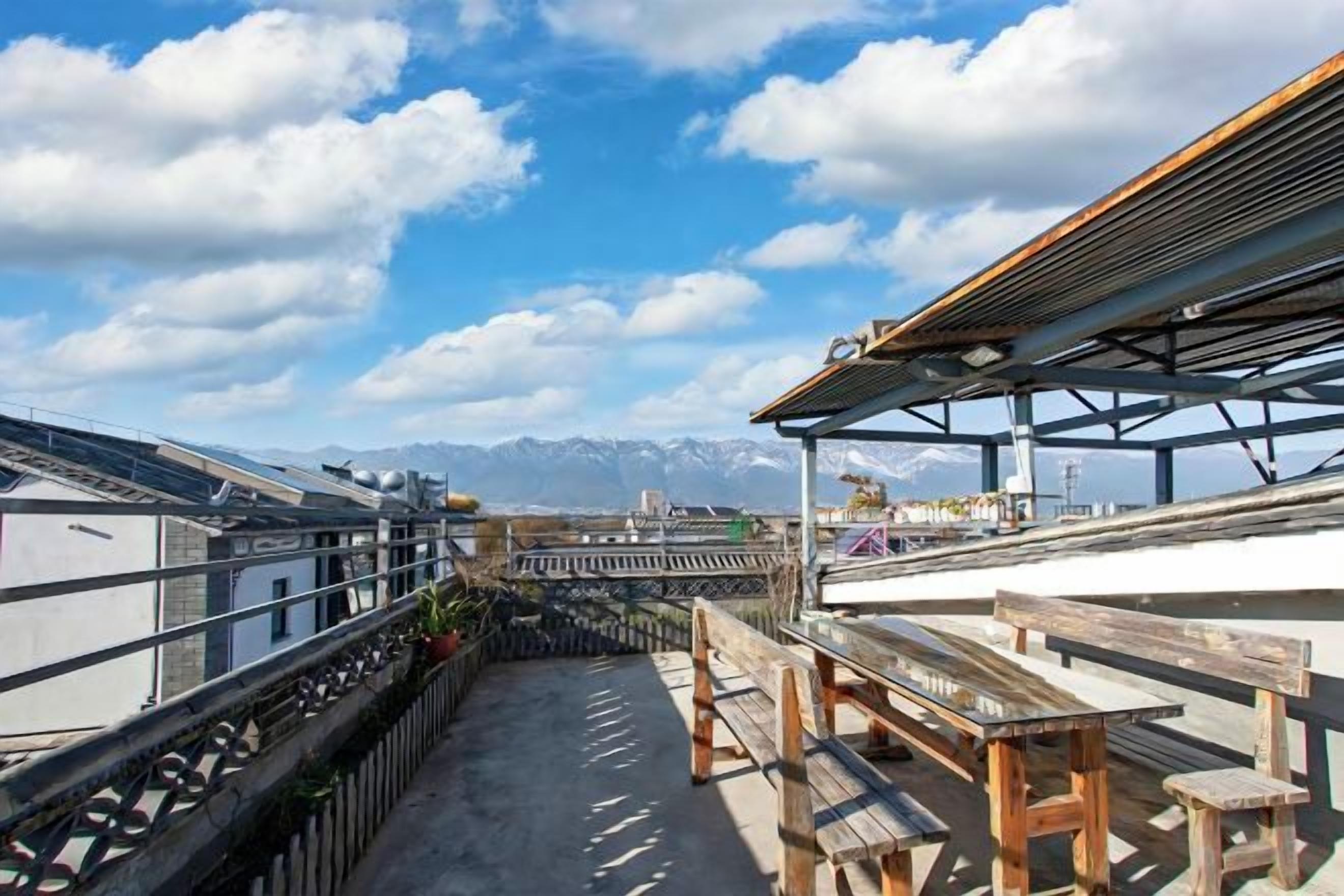 A rooftop terrace with a view of mountains, wooden benches, and a metal railing.
