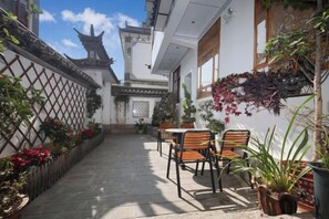 A courtyard with a traditional Balinese architectural style, featuring a tiled floor, wooden chairs, and potted plants.