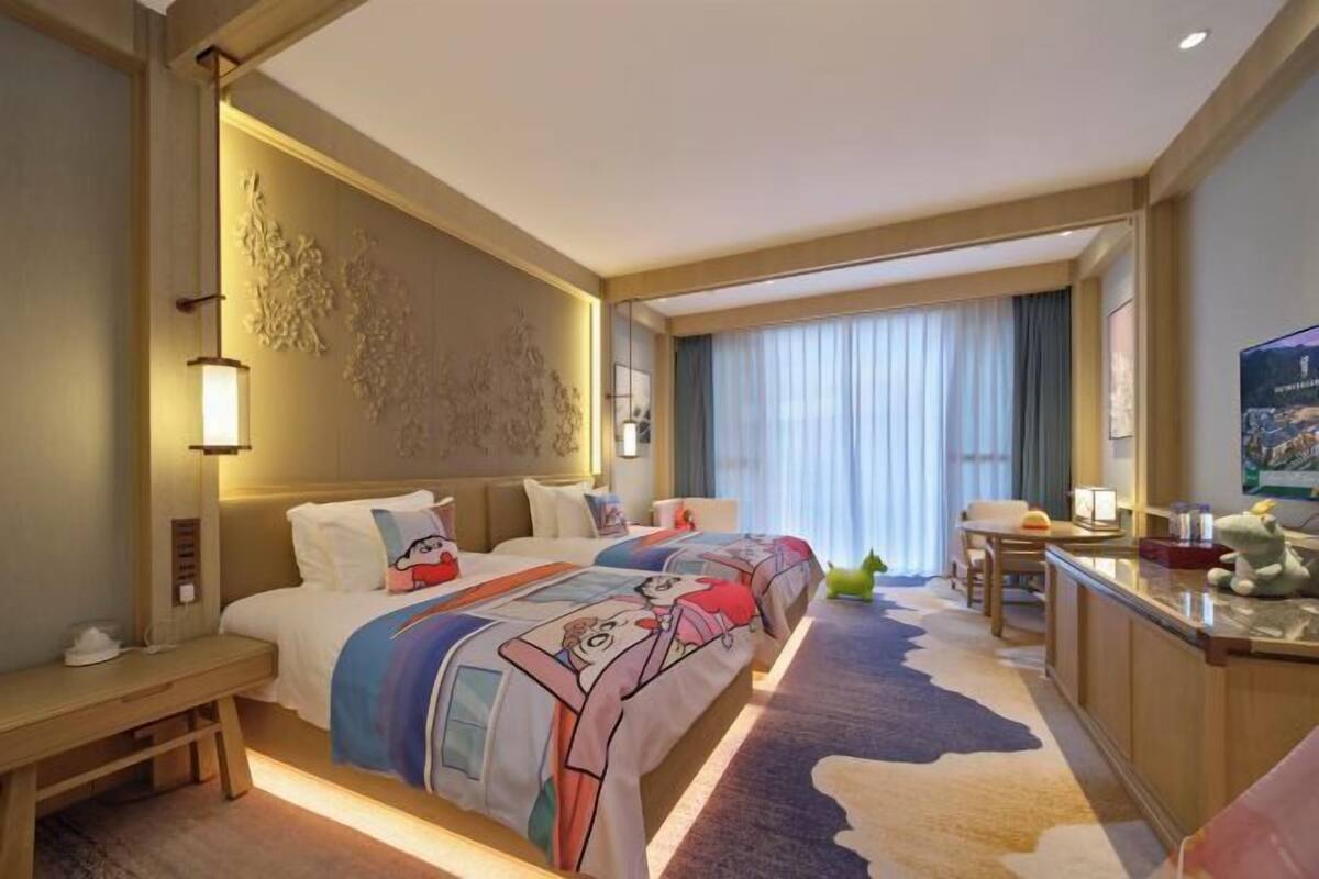 Hotelkamer met twee bedden, een bureau, een stoel, een televisie en een groot raam met gordijnen.
