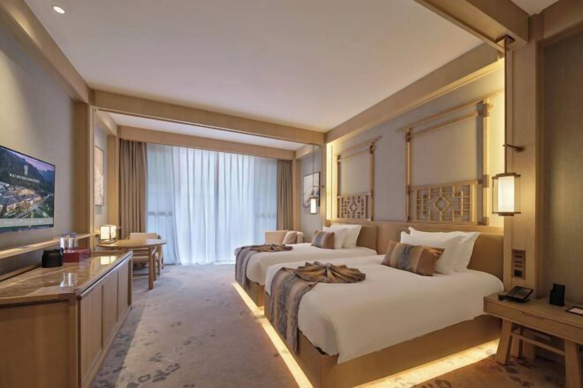 Een hotelkamer met twee bedden, een bureau, een televisie en een groot raam met gordijnen.