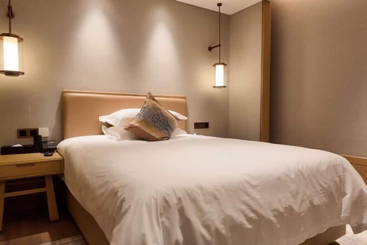 Een hotelkamer met een bed, nachtkastje, lamp en een wandlamp.