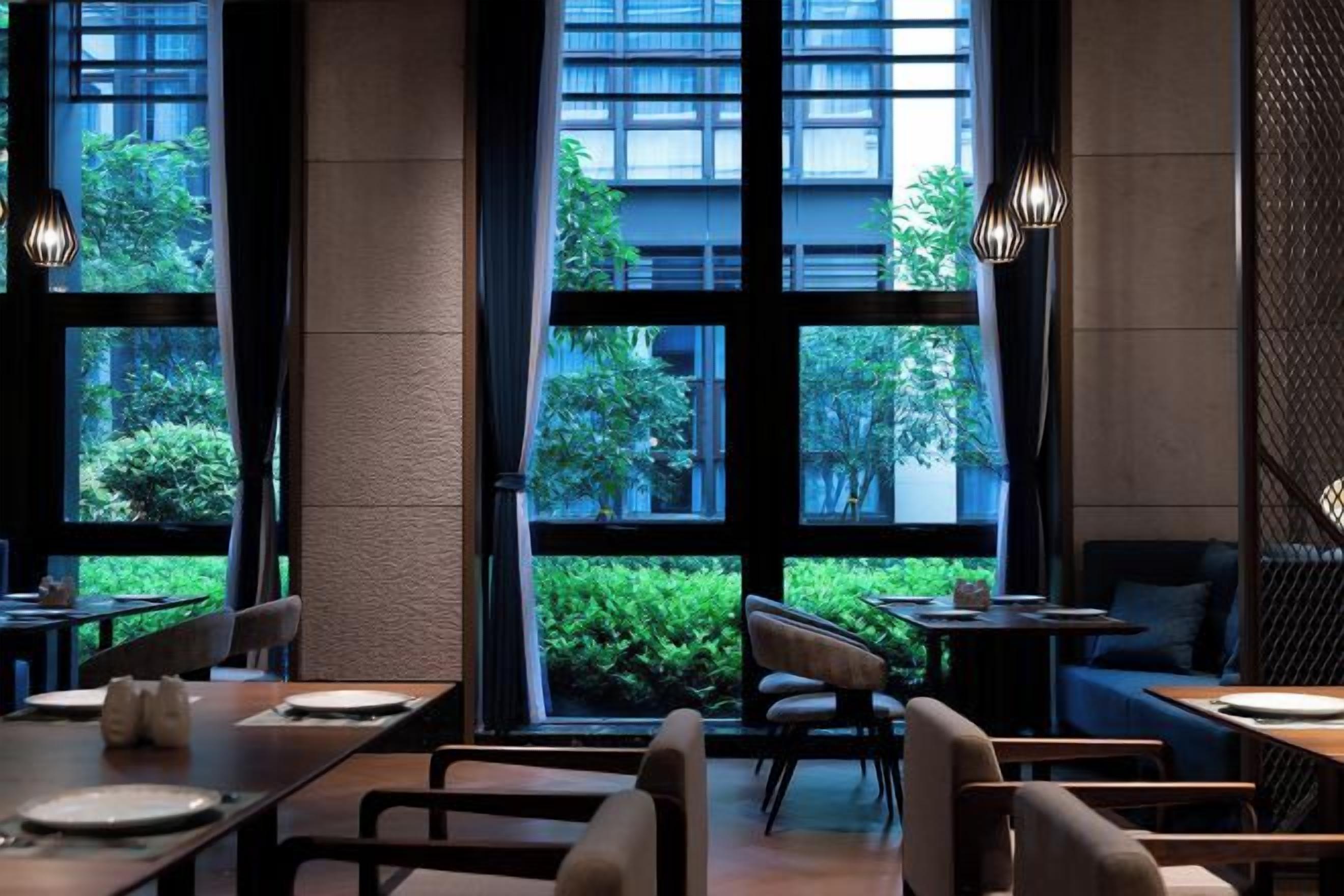 A modern restaurant with large windows, indoor seating, and a view of greenery.