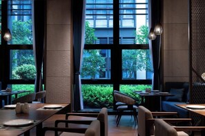En moderne restaurant med store vinduer, indendørs siddepladser og udsigt til grønne områder.