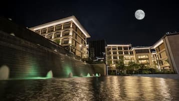 A nighttime view of a building with a water feature in front, a full moon in the sky, and illuminated windows.