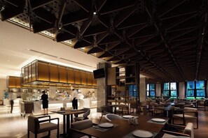A spacious restaurant with high ceilings, modern furniture, and a kitchen area visible in the background.
