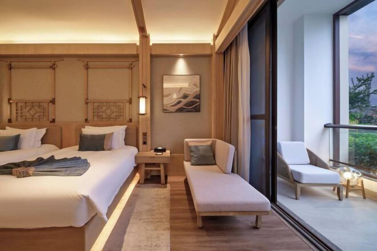 Een hotelkamer met een bed, een bank, een kleintje tafeltje en een balkon met een stoel.