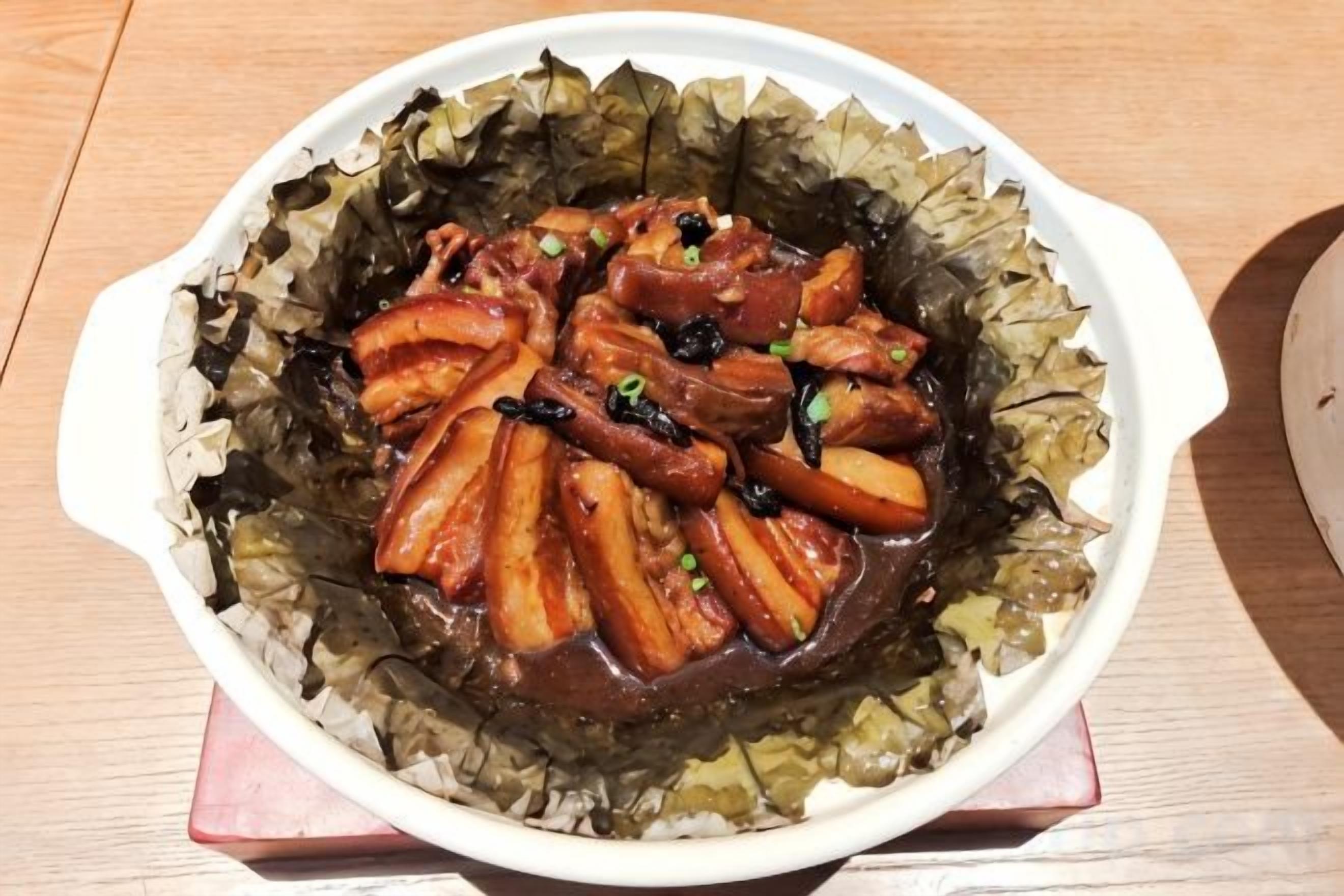 A dish of glazed meat in a leaf-lined bowl.