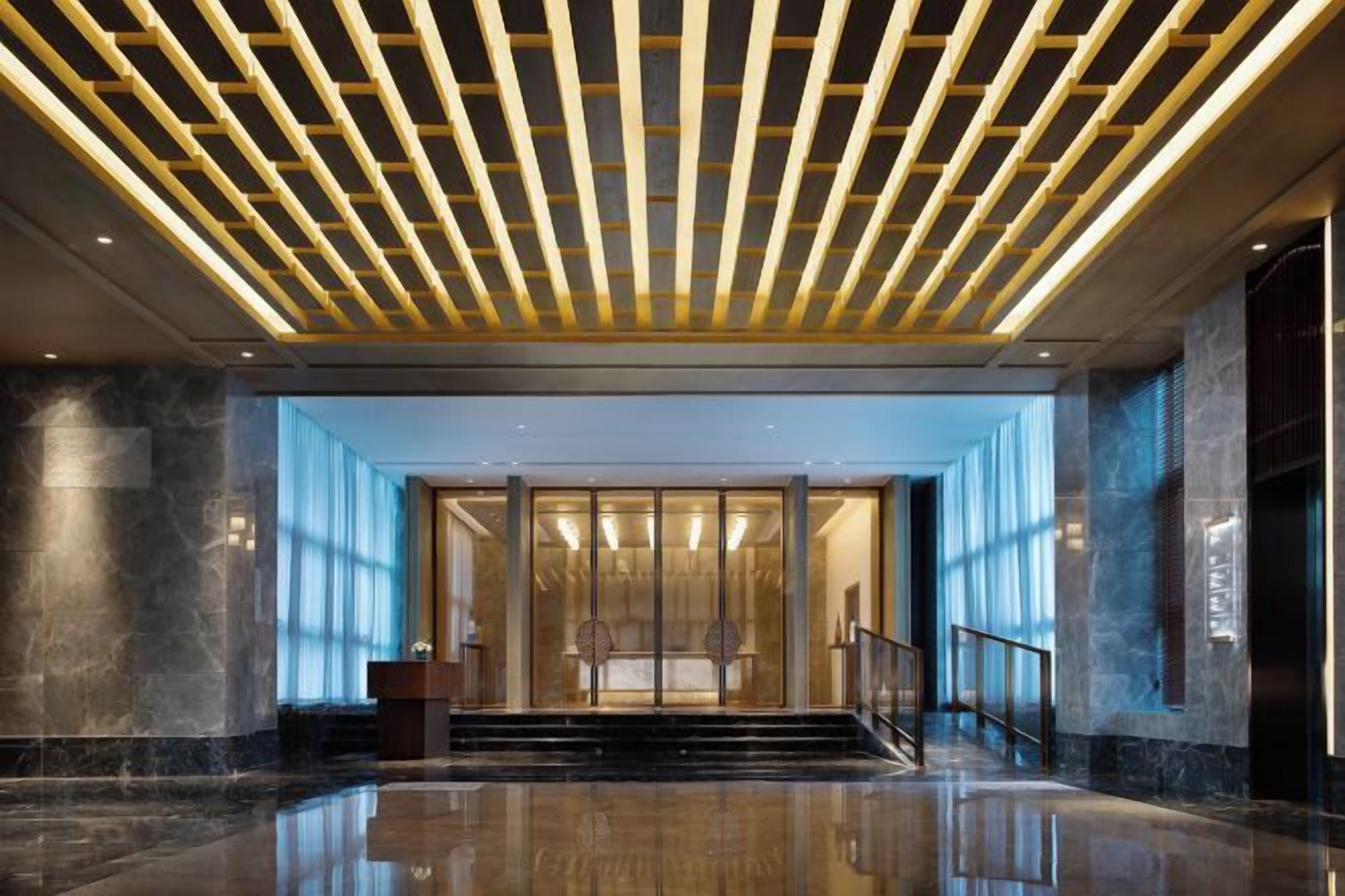 Un moderno vestíbulo con entrada de vidrio, una escalera y un techo con luminarias lineales.