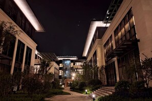 A nighttime view of a building with a central atrium, surrounded by trees and illuminated by artificial lighting.