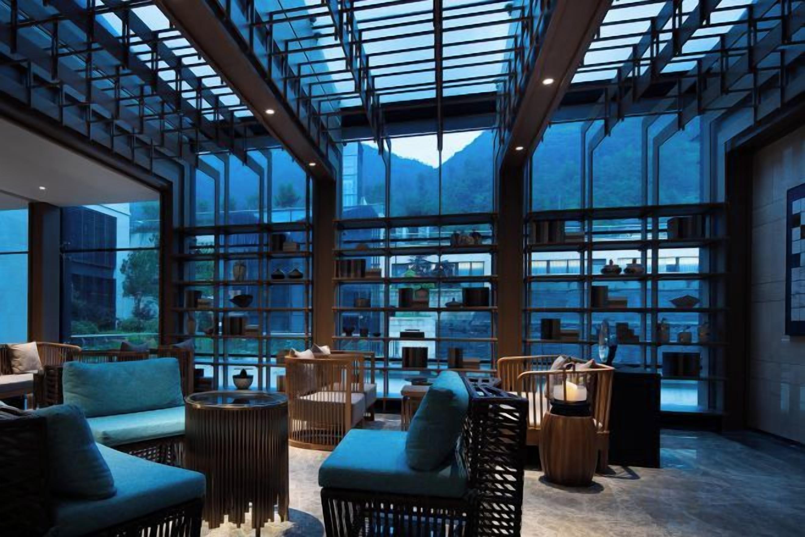 A spacious indoor area with a glass ceiling, wicker furniture, and a view of a mountainous landscape.