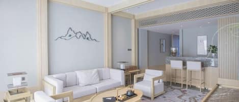 Quarto de hotel moderno com sofá branco, mesa de centro de madeira e área de cozinha com banquetas.