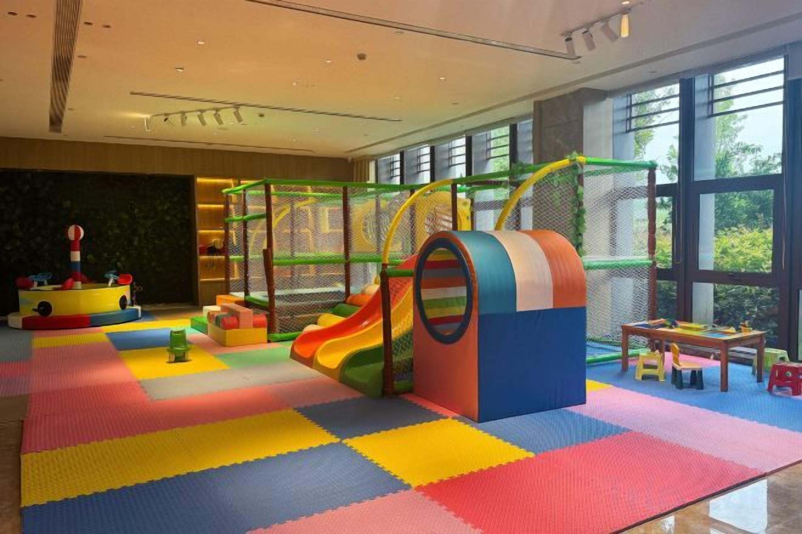 Zona de juegos infantiles con tobogán, colchonetas blandas y estructura para escalar.